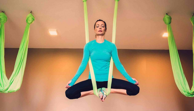 A woman does easy pose hanging from silks