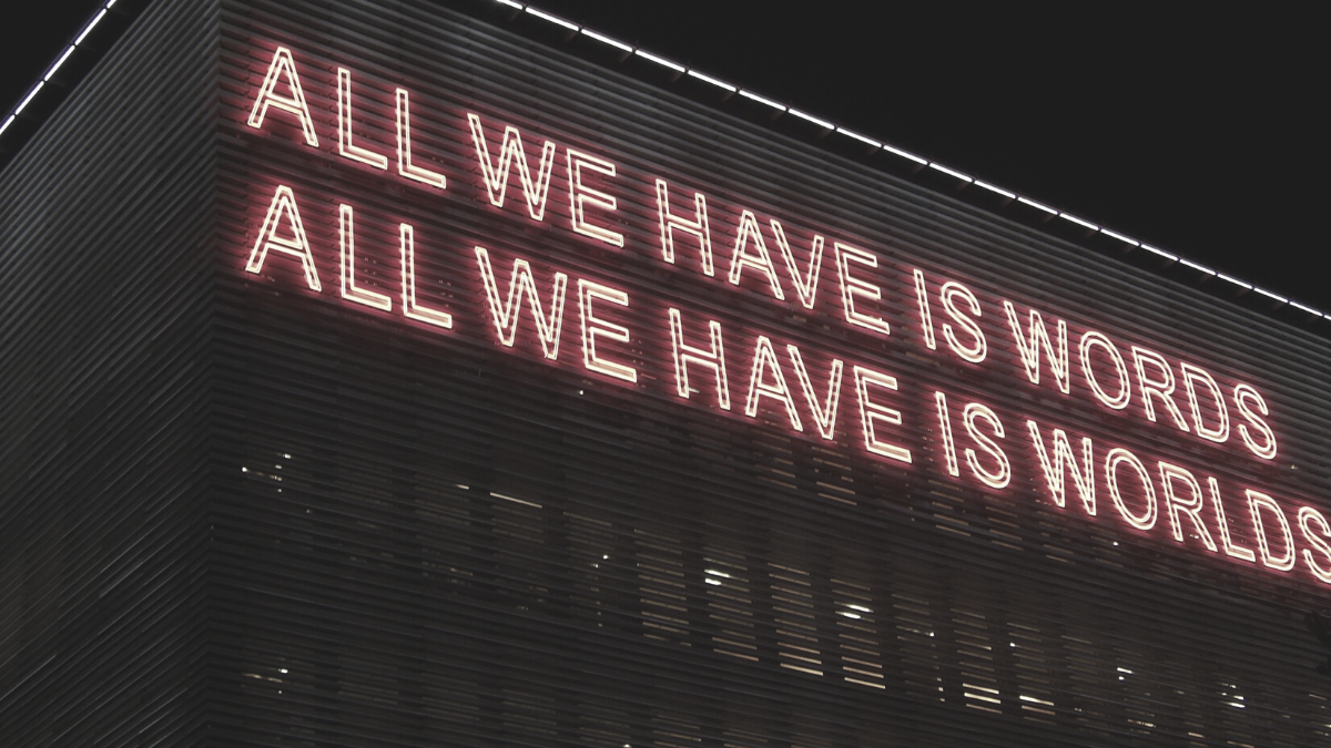 Neon sign reading ALL WE HAVE IS WORDS, ALL WE HAVE IS WORLDS